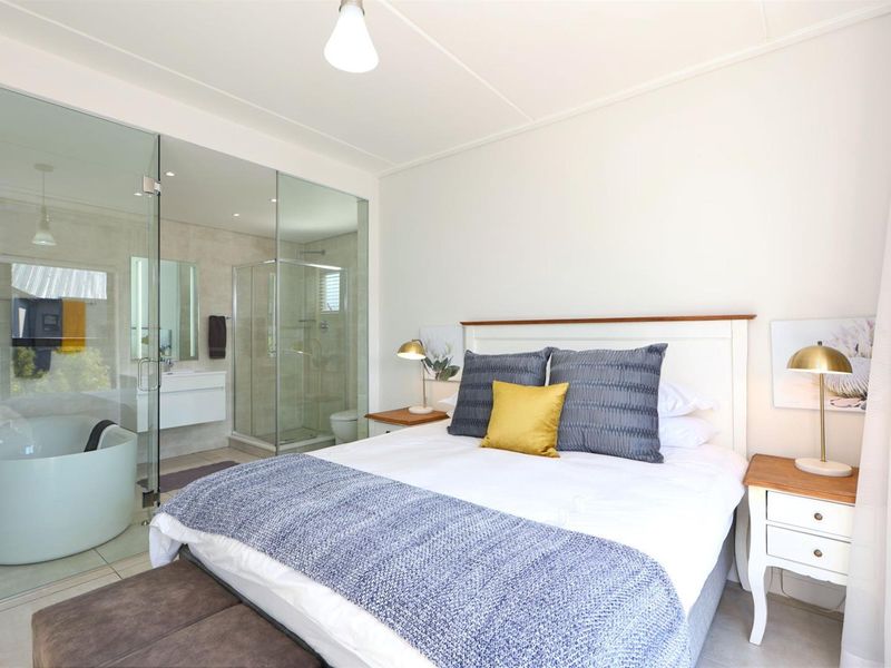 Modern bedroom featuring an integrated en-suite bathroom with a glass partition, freestanding bathtub, glass shower enclosure, and a sleek wall-mounted vanity.