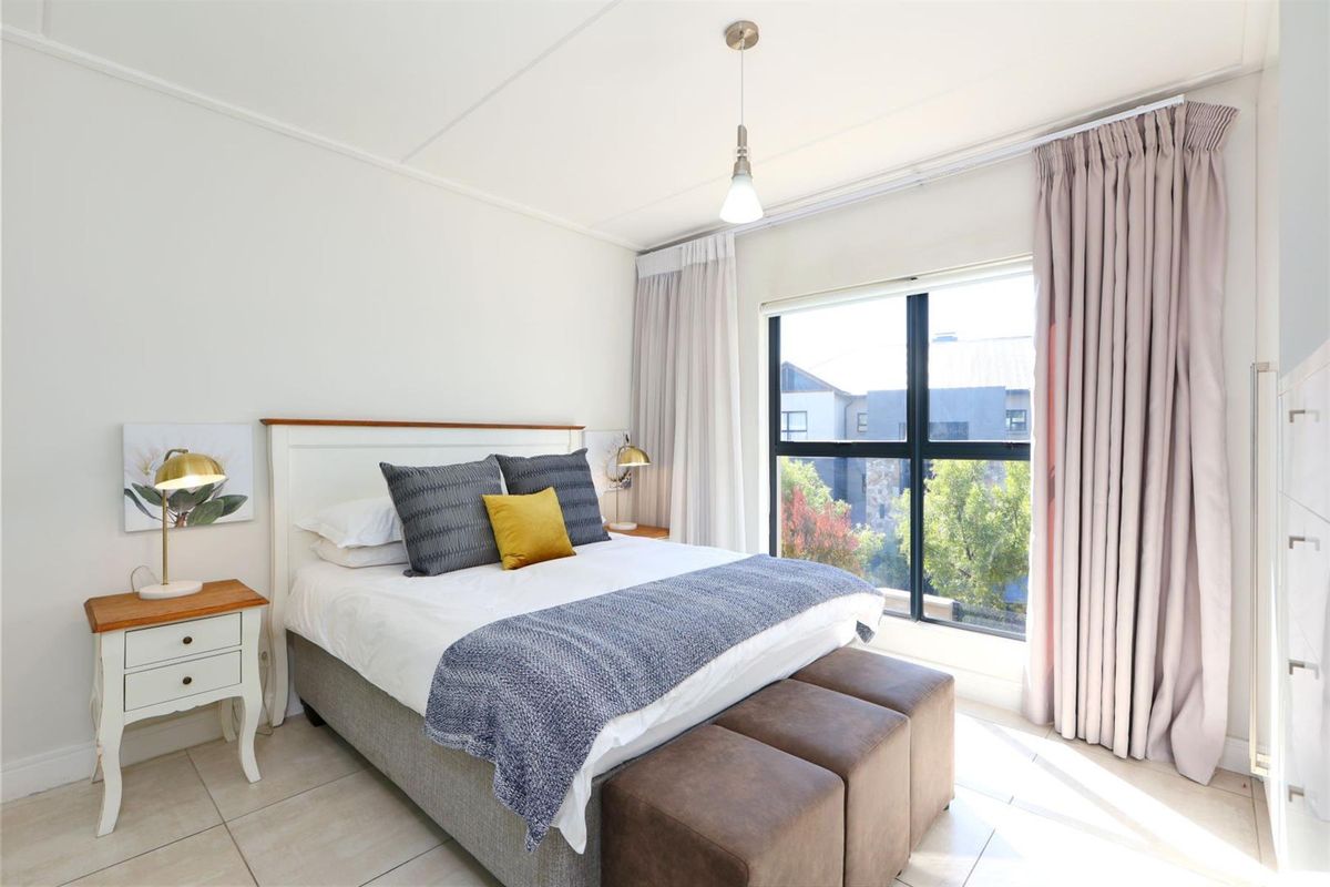 A bright and well-maintained bedroom featuring large windows with curtain tracks, neutral tiled flooring, and modern pendant lighting.