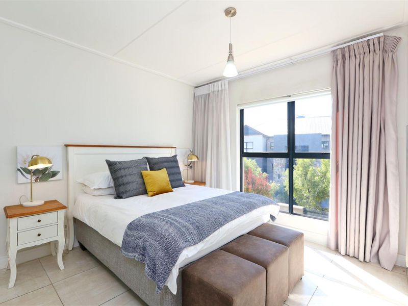 A bright and well-maintained bedroom featuring large windows with curtain tracks, neutral tiled flooring, and modern pendant lighting.