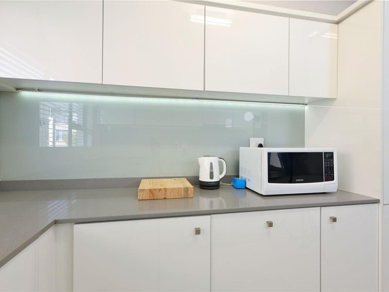 Modern kitchen featuring sleek white cabinetry, stone countertops, and a contemporary glass splashback with integrated under-cabinet lighting.