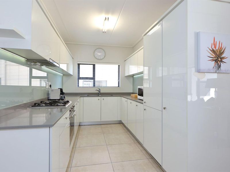 Modern galley-style kitchen featuring high-gloss white cabinetry, stone countertops, integrated gas hob, built-in oven, and a sleek glass splashback.