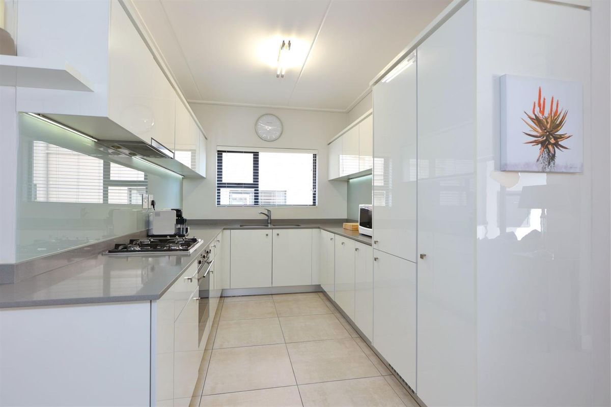 Modern galley-style kitchen featuring high-gloss white cabinetry, stone countertops, integrated gas hob, built-in oven, and a sleek glass splashback.