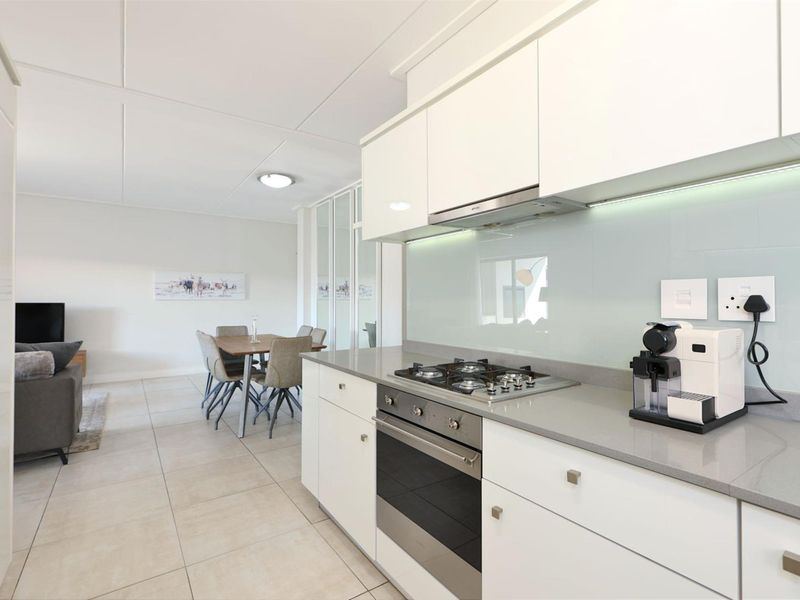 Modern open-plan kitchen featuring sleek white cabinetry, stone countertops, integrated gas hob, and oven, flowing seamlessly into the dining and living area.