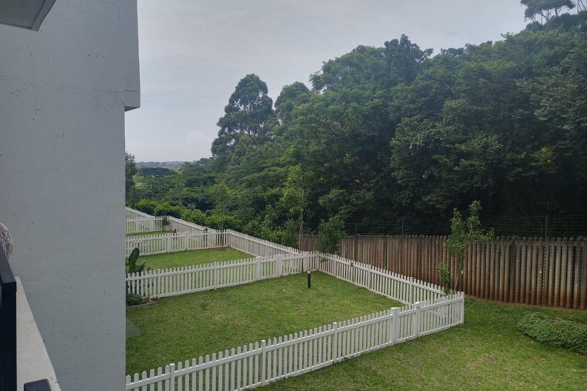 A view of the rear garden area featuring manicured lawns, white picket fencing, and a secure perimeter with electric fencing and mature trees.