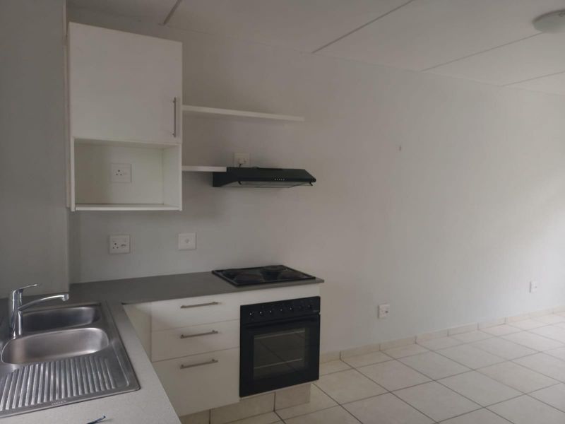 A functional, empty kitchen featuring white cabinetry, a stainless steel sink, built-in oven, electric hob, and tiled flooring.