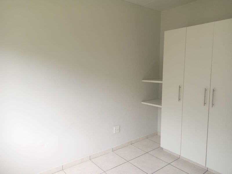 A clean, empty bedroom featuring neutral tiled flooring and a white built-in wardrobe with integrated shelving.