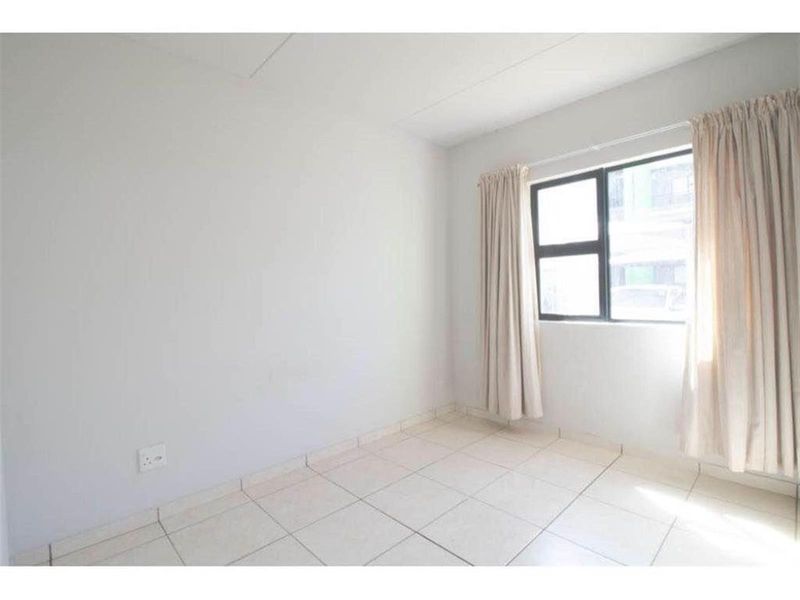 A bright, empty bedroom featuring neutral tiled flooring and a large aluminium-framed window, providing a clean canvas for personalization.