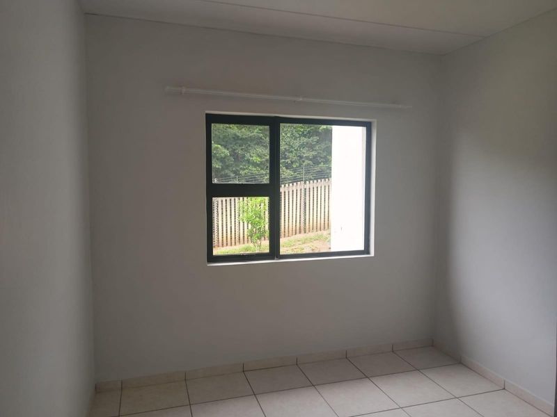 A clean, empty bedroom featuring neutral tiled flooring and a modern aluminium window frame, providing a blank canvas for interior design.
