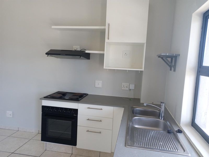 A clean, functional kitchen featuring built-in cabinetry, a stainless steel double sink, electric hob, oven, and extractor fan with neutral tiled flooring.