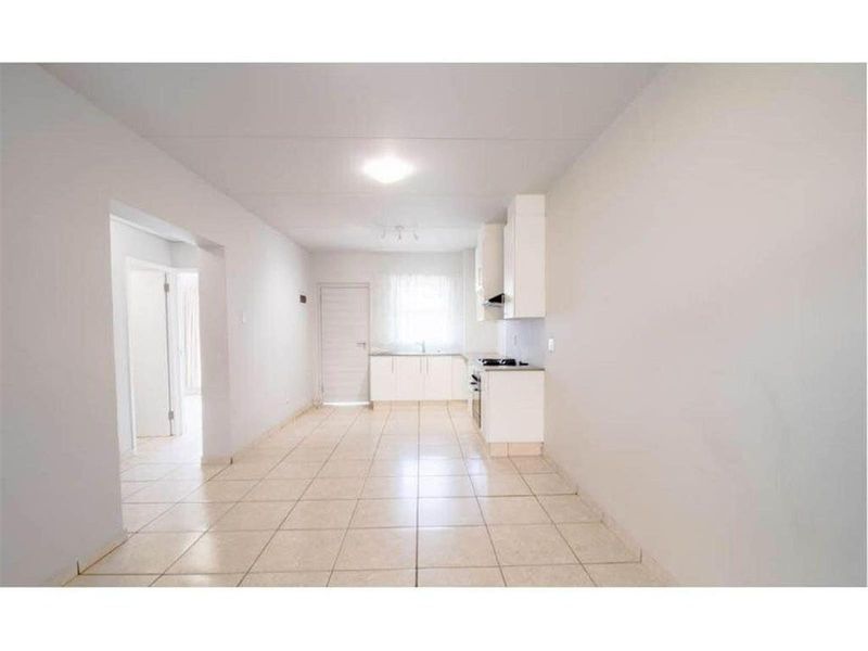 An open-plan living and kitchen area featuring tiled flooring, white built-in cabinetry, and integrated cooking appliances in a clean, vacant space.