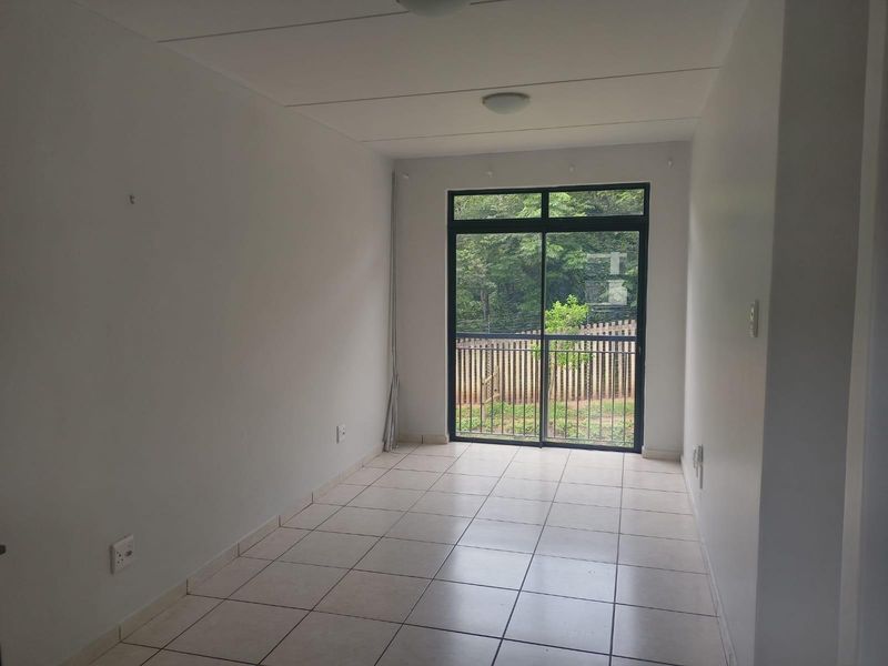 A bright, empty living area featuring neutral tiled flooring and a large sliding glass door that provides natural light and garden views.
