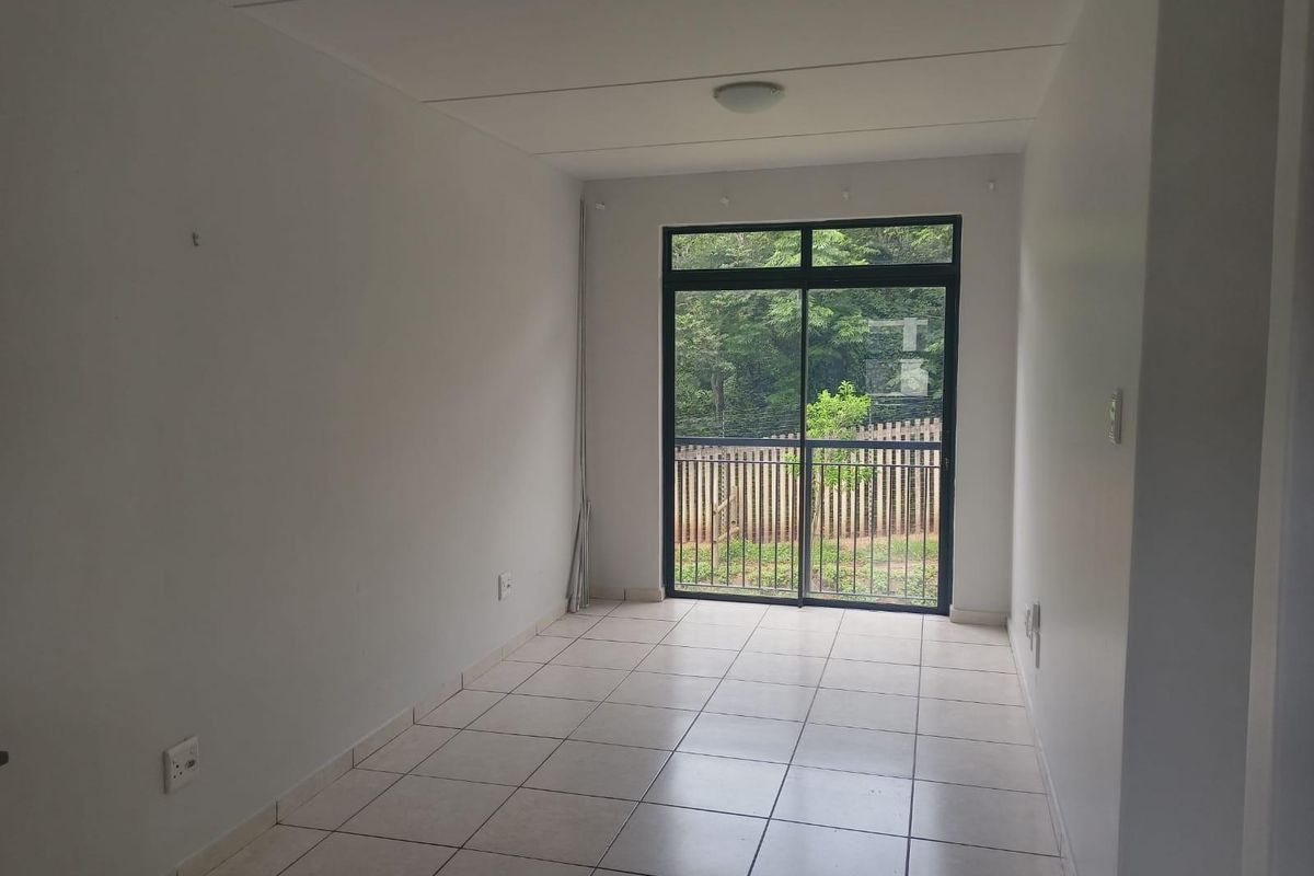 A bright, empty living area featuring neutral tiled flooring and a large sliding glass door that provides natural light and garden views.