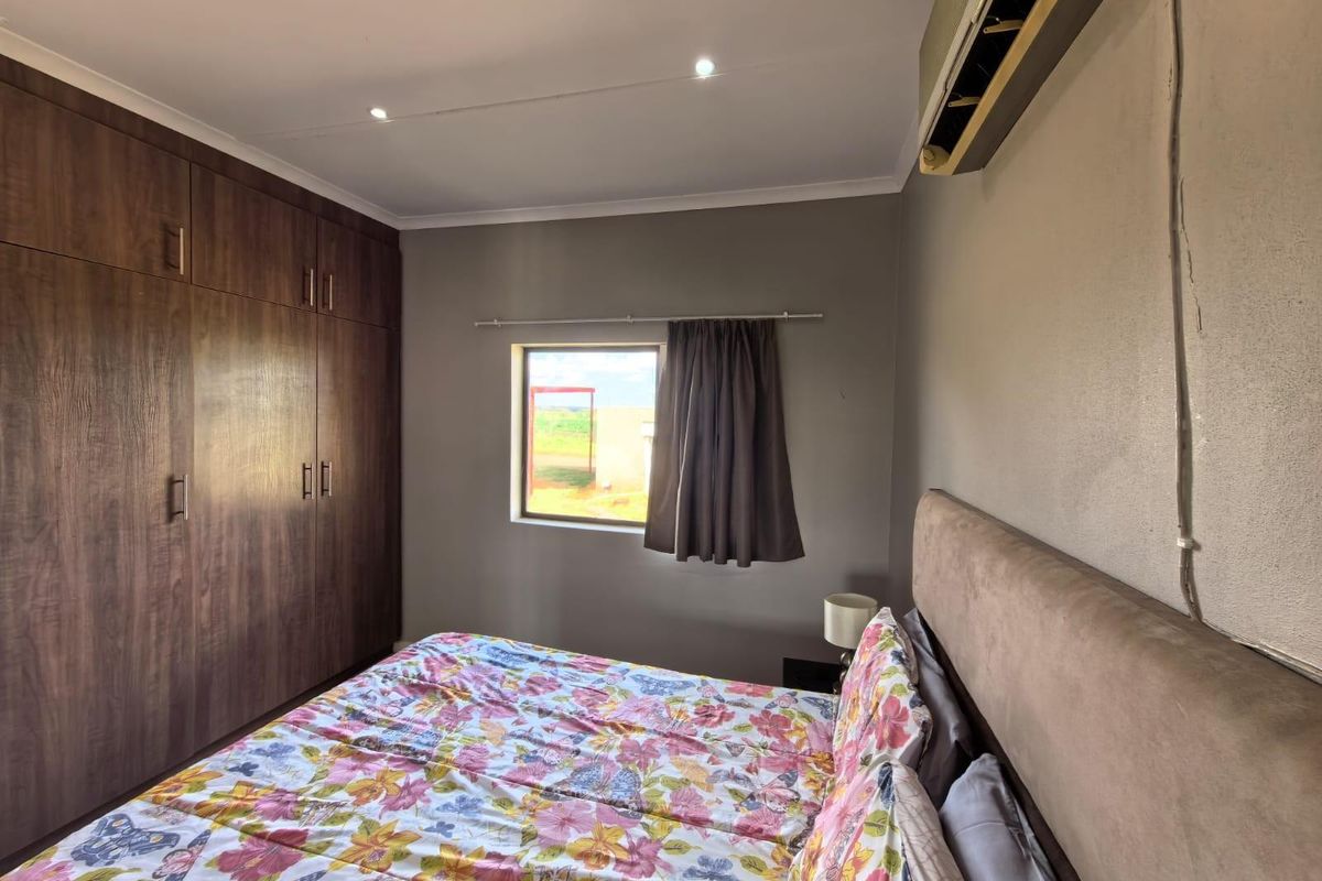 A bedroom featuring built-in wooden cupboards, recessed ceiling lighting, and a wall-mounted air conditioning unit.