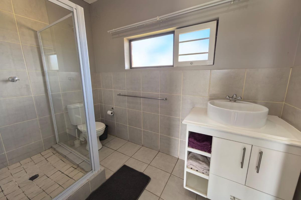 A functional bathroom featuring a glass-enclosed shower, a modern vessel sink vanity, and neutral wall and floor tiling.