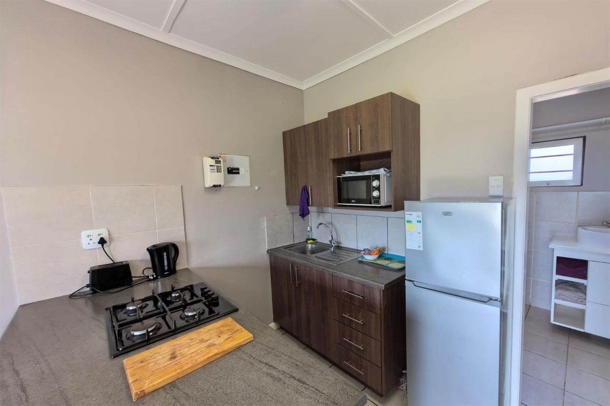 Compact kitchen area featuring dark wood cabinetry, a built-in gas hob, stainless steel sink, and tiled splashbacks, with an adjacent bathroom visible.