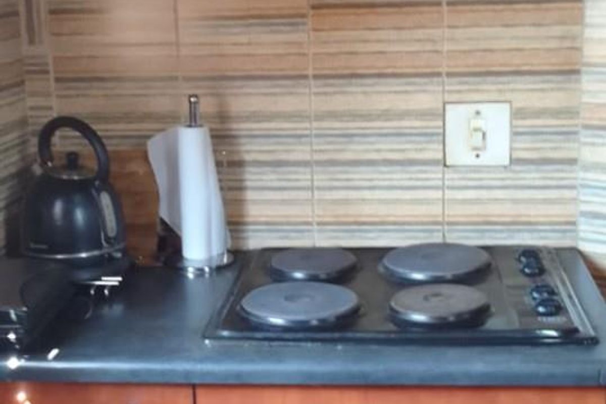 A compact kitchen area featuring wooden cabinetry, a built-in electric oven, a four-plate electric hob, and a black extractor fan.