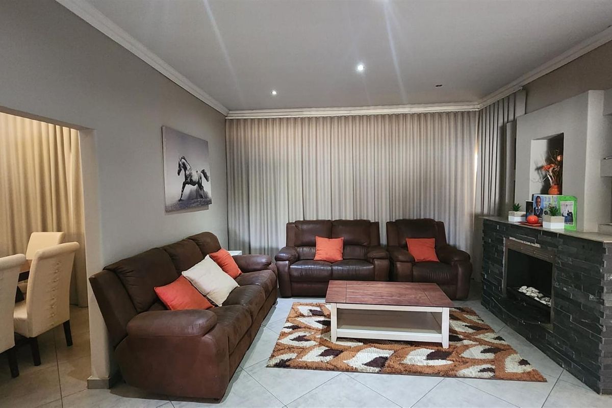 A comfortable living room featuring a prominent stone-clad fireplace, tiled flooring, and recessed ceiling lighting, with an adjacent dining area visible.