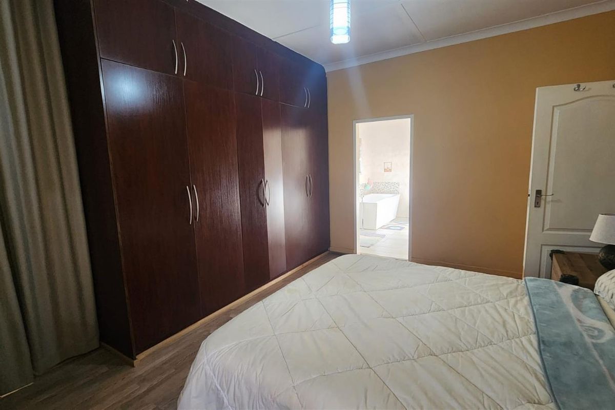 A bedroom featuring extensive dark wood built-in cupboards, laminate flooring, and direct access to an adjoining bathroom.