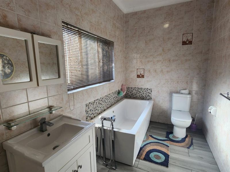 A functional bathroom featuring a vanity, a modern freestanding bathtub, and a toilet, finished with neutral wall and floor tiling.