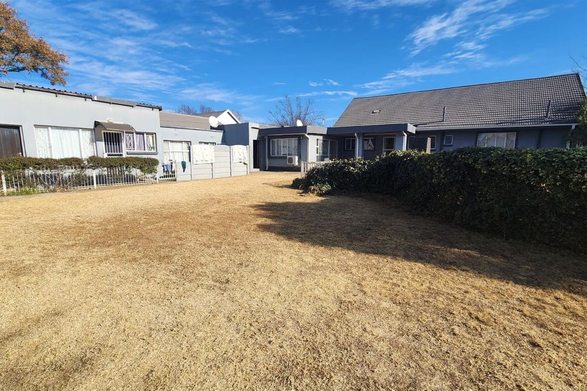 A view of the rear exterior of the house featuring a large lawn, plastered walls, and a tiled roof structure.