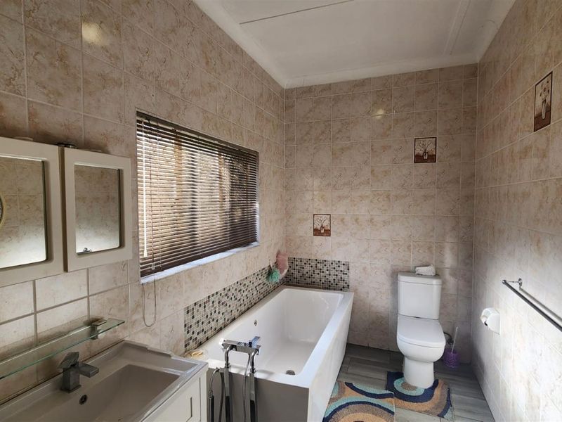 A functional bathroom featuring a built-in bathtub, toilet, and vanity basin with neutral wall tiling and modern floor finishes.