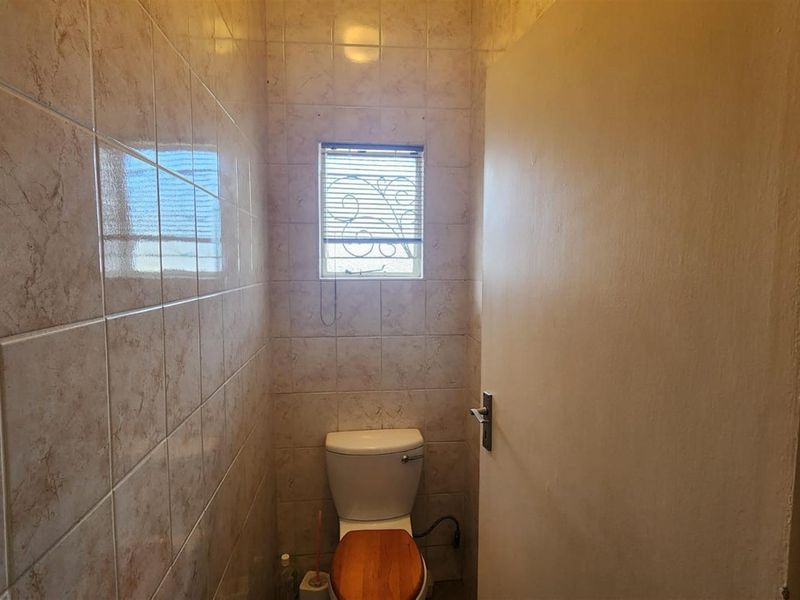 A compact guest bathroom featuring full-height ceramic wall tiling, a standard toilet, and a small window with security bars.