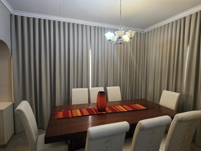 A formal dining room featuring an elegant archway entrance, ceiling cornice detailing, and full-length wall curtains providing a soft, finished aesthetic.