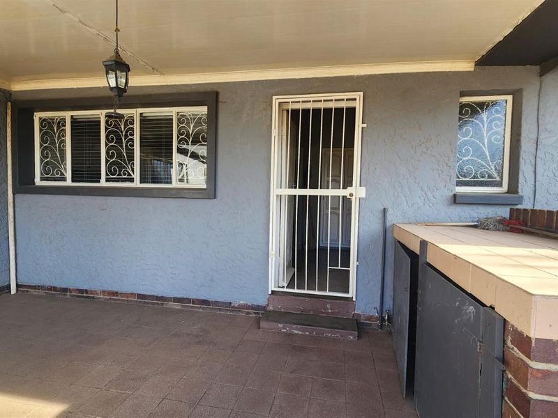 A covered patio area featuring tiled flooring, a built-in braai, and security gates, providing a functional outdoor entertainment space.