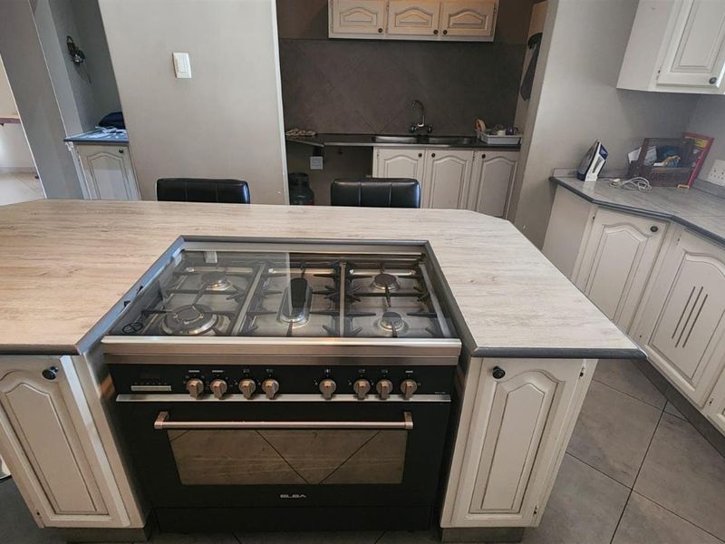 A functional kitchen featuring a central island with a built-in gas hob and oven, ample cabinetry, and tiled flooring.