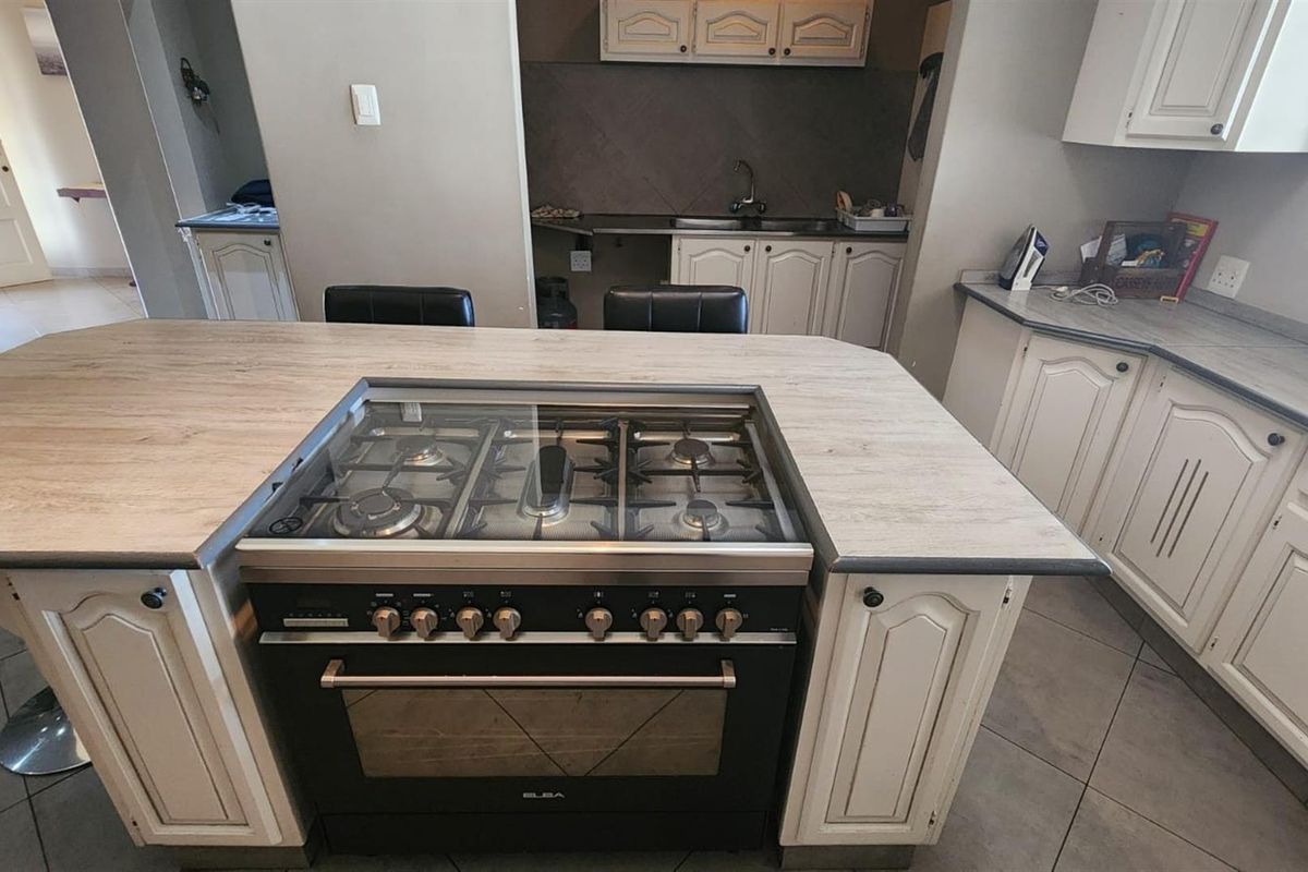 A functional kitchen featuring a central island with a built-in gas hob and oven, ample cabinetry, and tiled flooring.