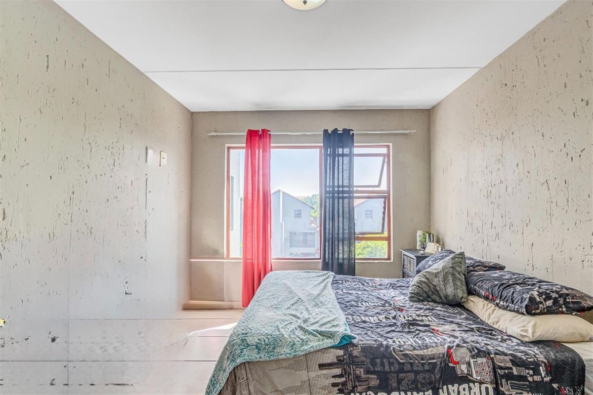 A bedroom featuring a large window with natural light, textured wall finishes, and tiled flooring.