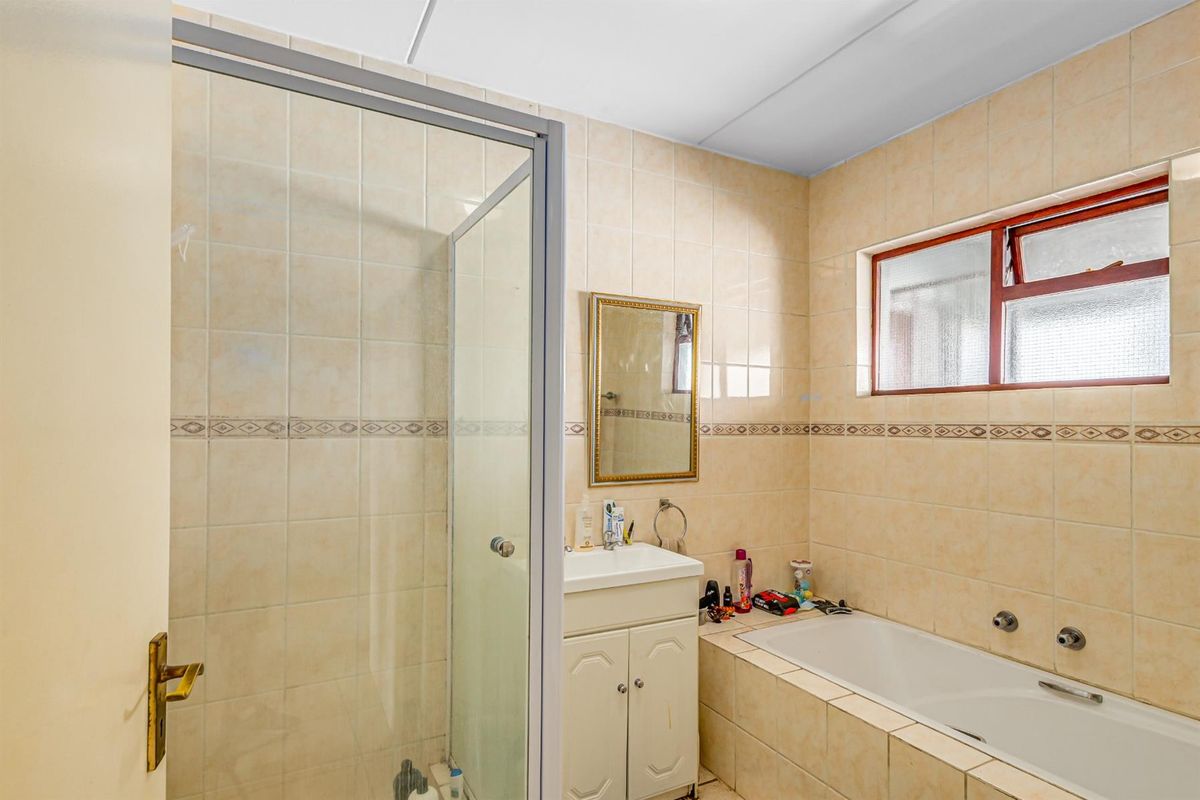 A functional bathroom featuring a built-in bathtub, a separate glass-enclosed shower, and a vanity unit with tiled walls throughout.