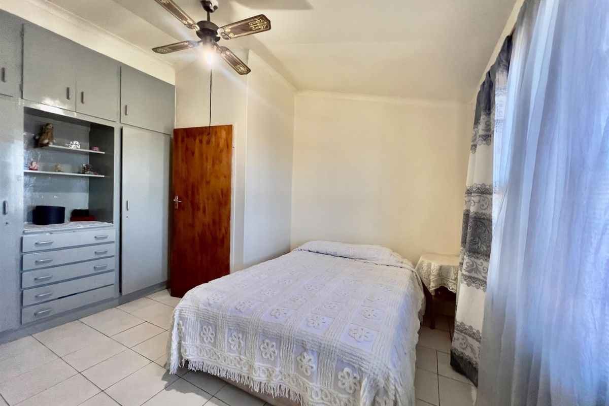 A functional bedroom featuring built-in grey cabinetry, tiled flooring, and a ceiling fan, offering a practical layout with natural light.