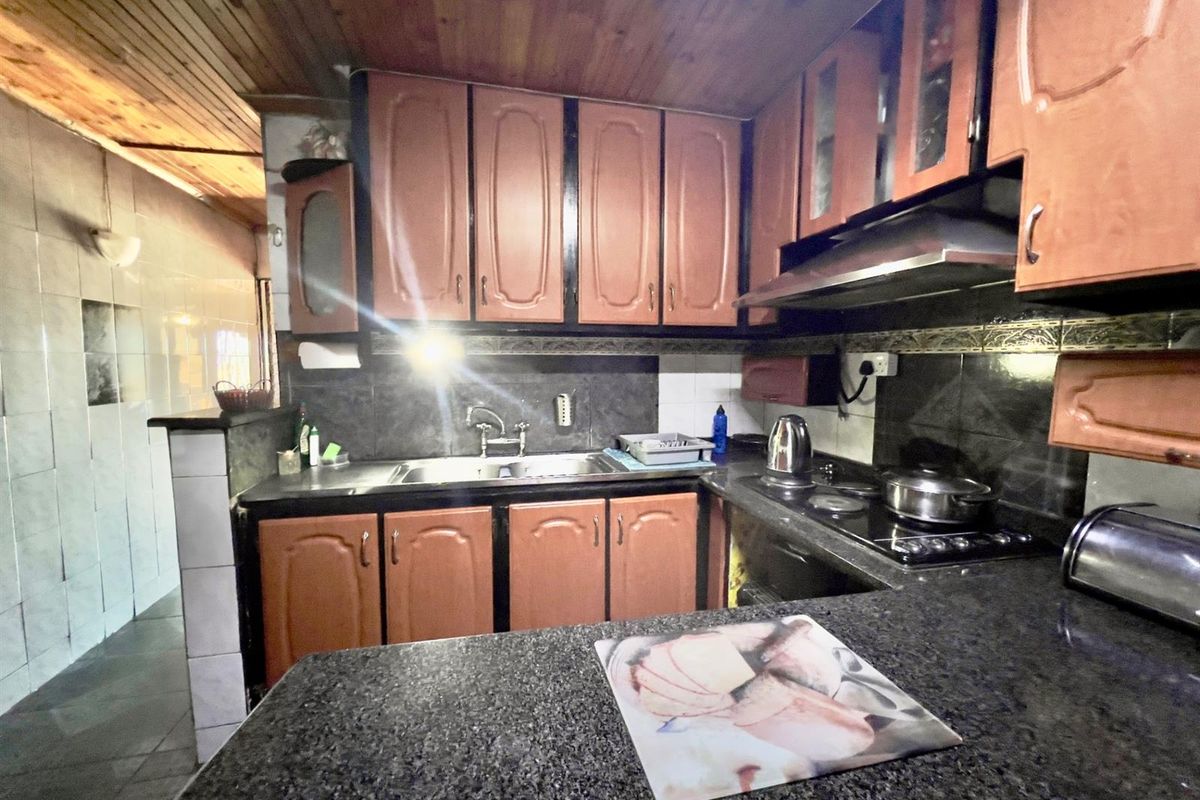 A functional kitchen featuring dark granite countertops, wooden cabinetry, a built-in hob, and an extractor fan, with a wood-paneled ceiling.