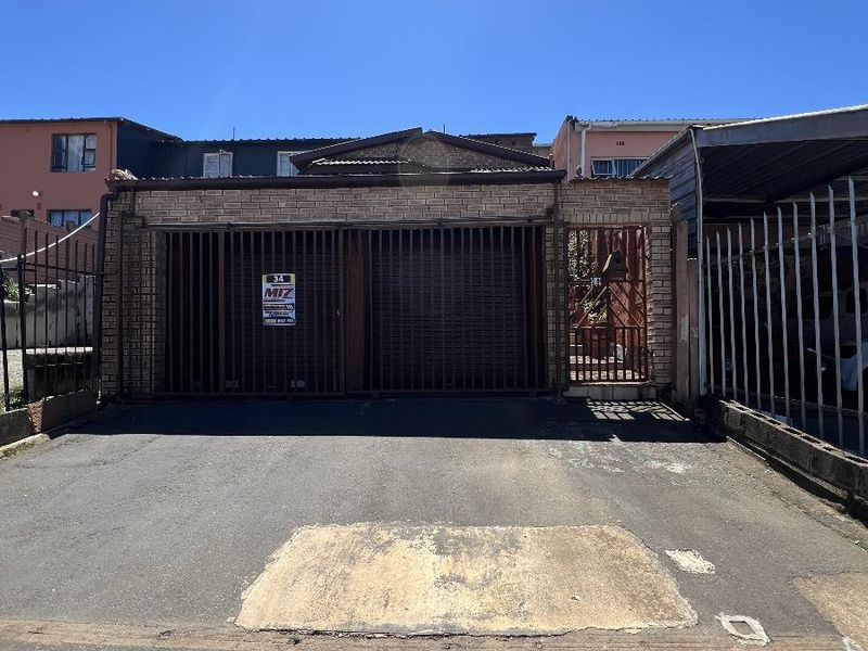 Front exterior view of the property featuring a brick facade, secure metal gate entrance, and an asphalt driveway with visible surface wear.