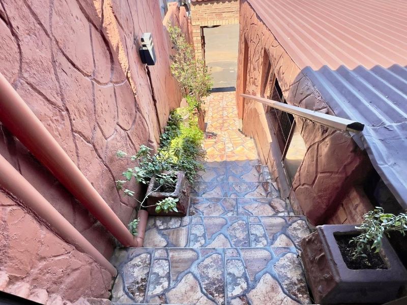 An exterior staircase featuring stone-look tiled steps, textured masonry walls, and a metal handrail, leading down towards a lower level entrance.