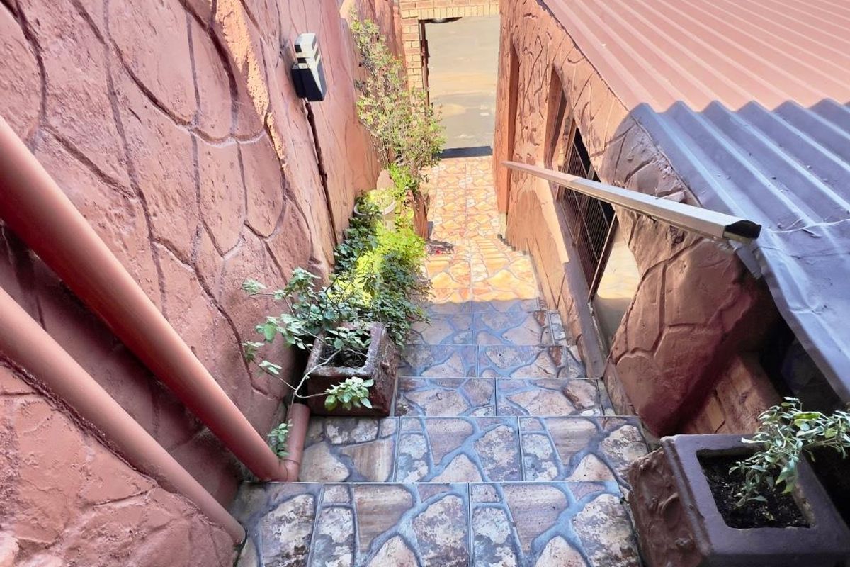 An exterior staircase featuring stone-look tiled steps, textured masonry walls, and a metal handrail, leading down towards a lower level entrance.