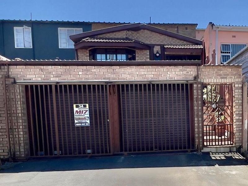 Front exterior view of the property featuring a double garage with metal security gates and a brick facade.