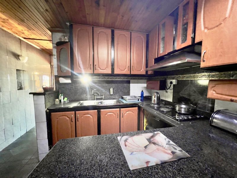 A functional kitchen featuring dark granite countertops, wooden cabinetry, a built-in hob, and an extractor fan, with a wood-paneled ceiling.
