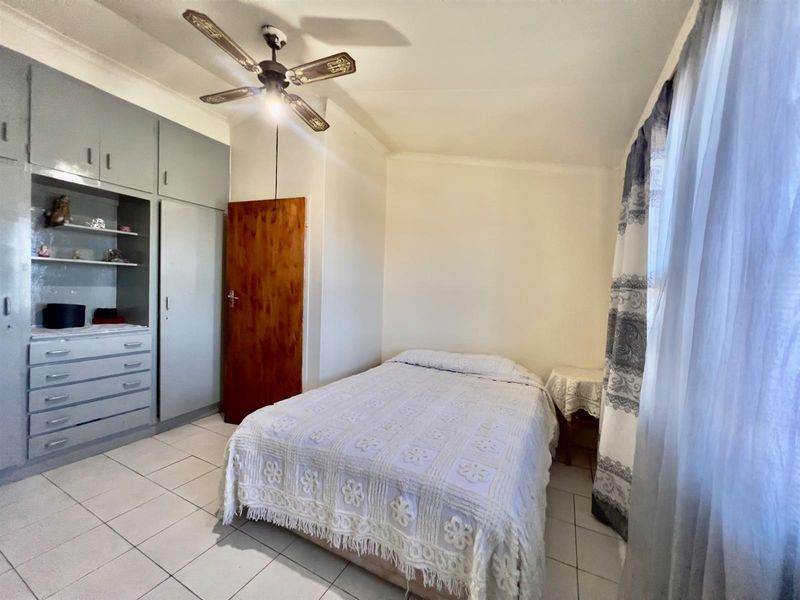 A functional bedroom featuring built-in grey cabinetry, tiled flooring, and a ceiling fan, offering a practical layout with natural light.