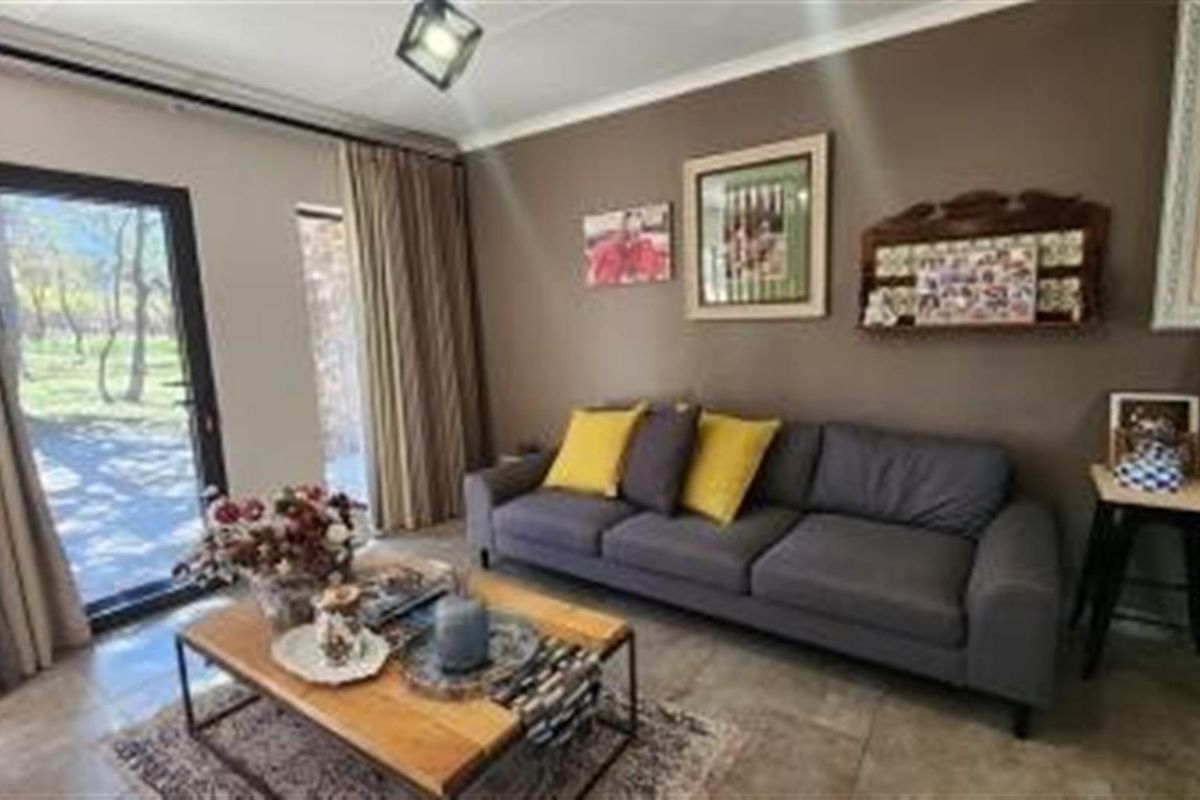A comfortable living room featuring tiled flooring, a modern light fixture, and large glass sliding doors providing natural light and access to the garden.