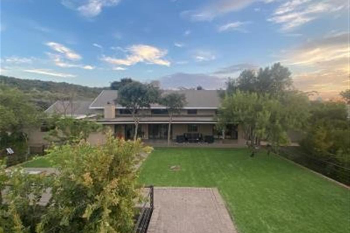 A view of the rear exterior of the property, featuring a spacious lawn, paved walkway, and a covered patio area.