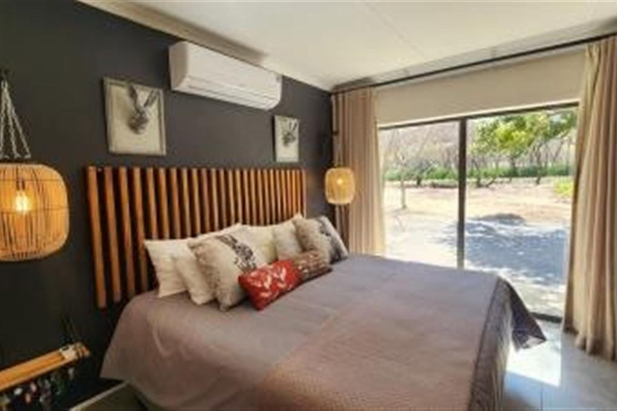 A well-appointed bedroom featuring a built-in wooden headboard, wall-mounted air conditioning unit, and large sliding glass doors providing natural light and garden views.