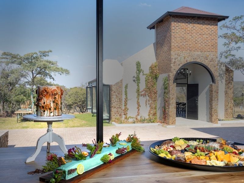 View from an interior space looking out towards a charming brick and stone building with an arched entrance and landscaped grounds.