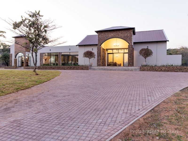 A well-maintained modern farmhouse-style property featuring stone cladding, a paved driveway, and a prominent arched entrance.