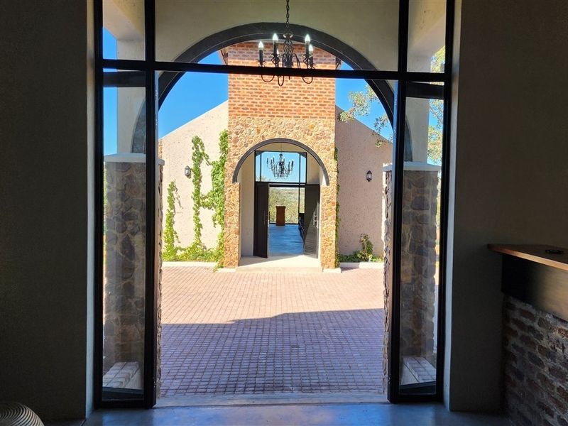 A view through a grand arched entrance looking out onto a paved courtyard and a secondary stone-clad building structure.