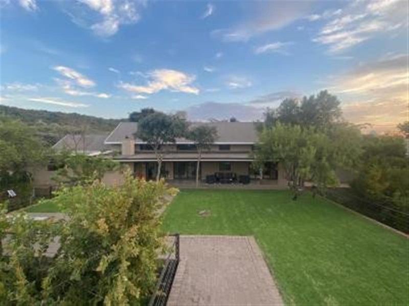 A view of the rear exterior of the property, featuring a spacious lawn, paved walkway, and a covered patio area.