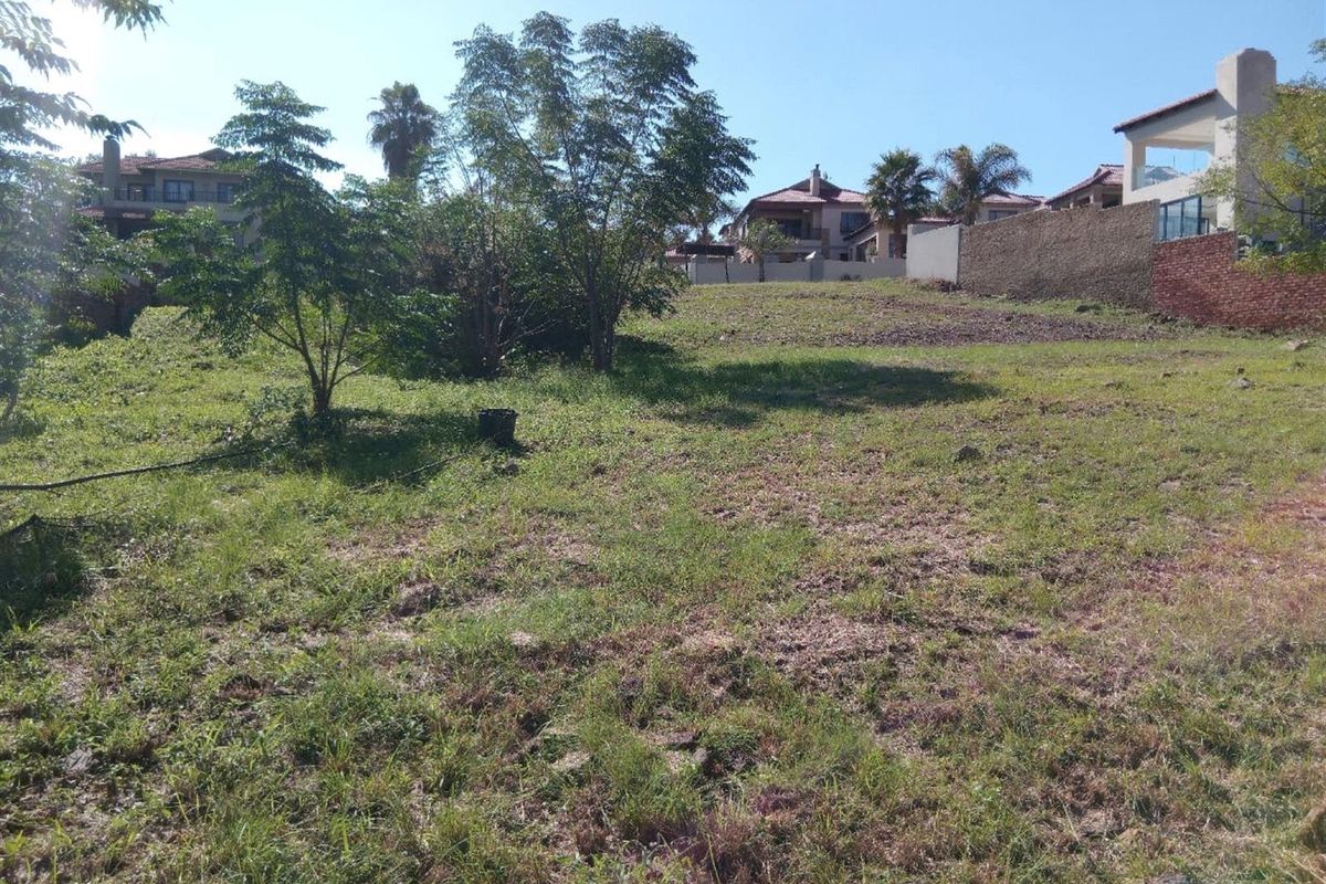 A vacant residential plot featuring a gentle slope, established trees, and surrounding boundary walls in a developed neighborhood.