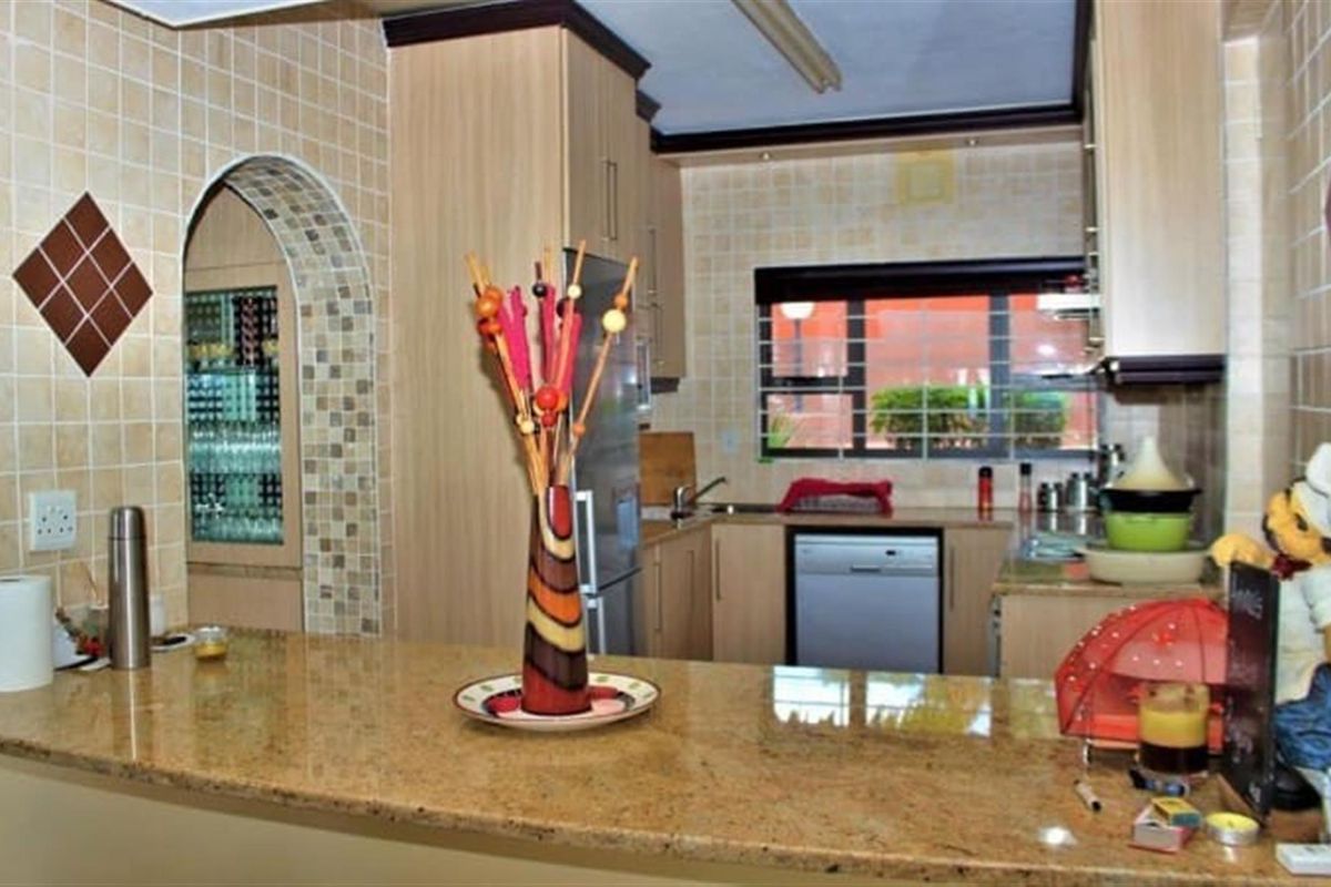 A functional kitchen featuring granite countertops, light wood cabinetry, and a tiled backsplash with an arched entryway leading to an adjacent space.