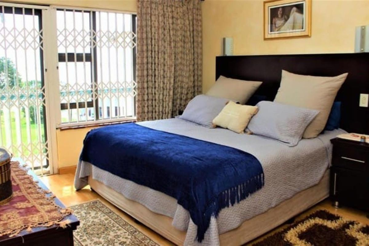 A comfortable bedroom featuring a built-in headboard, laminate flooring, and a sliding door with security gate leading to an outdoor area.